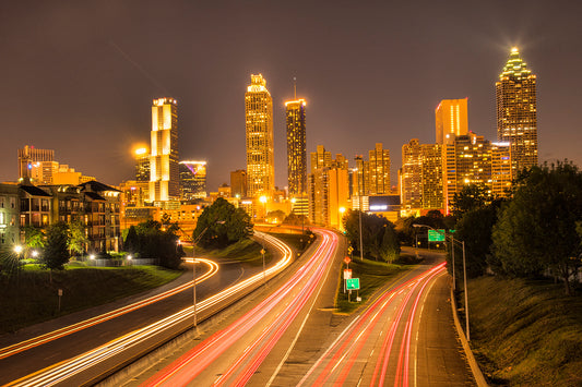 Night time view of the Atlanta skyline from the Jackson Street Bridge aglow with streaming headlight and taillight glows from passing cars make an awesome image for home or office display in either canvas or metal printing!